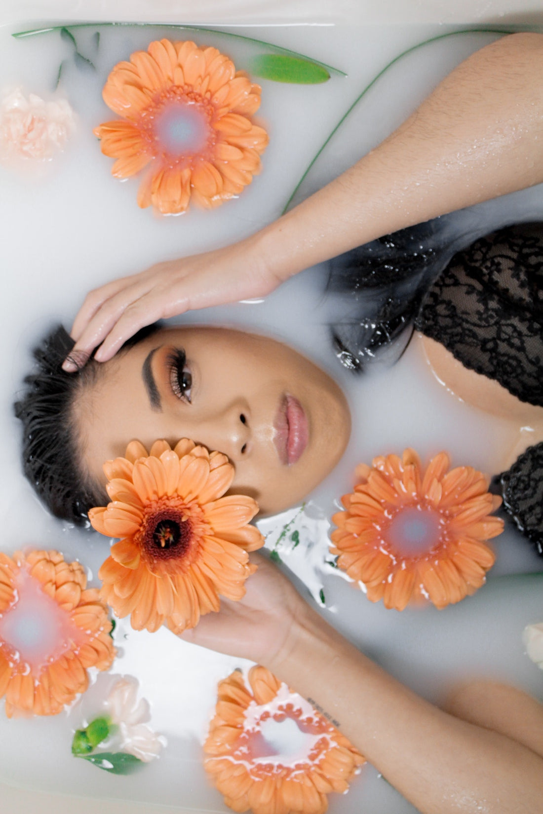 Beautiful ethnic woman laying in natural bath with flowers